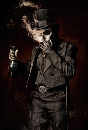 A young man in image of Baron Samedi, the Voodoo deity. Baron Saturday in black suit and top hat with a bottle of alcohol in hand. Day of the Dead (and Halloween) themeの写真素材