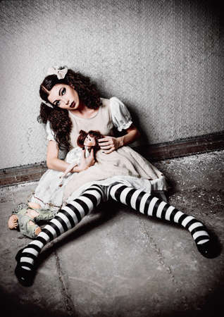 Strange lonely girl with dolls sitting in a dirty roomの写真素材