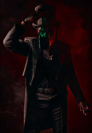 A young man in image of Baron Samedi, the Voodoo deity. Baron Saturday in black suit and top hat with a bottle of alcohol in hand. Day of the Dead (and Halloween) themeの写真素材