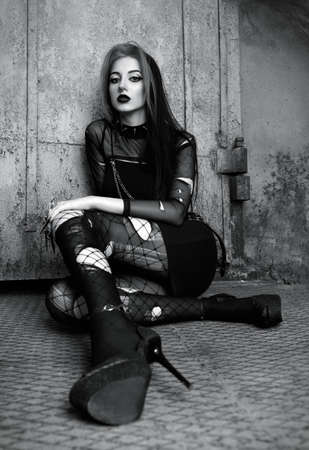 Outdoor portrait of lovely sad goth (deathrock) girl dressed in black skirt, holey blouse and pantyhose. Black and white. Dark beautyの写真素材