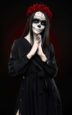 Young woman with calavera (sugar skull) makeup. The witch girl with muertos (muerte) greasepaint in black dress. Day of the dead (and Halloween) themeの写真素材