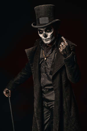 A young man in image of Baron Samedi, the Voodoo deity. Baron Saturday in black coat and top hat with stick in hand. Day of the Dead (and Halloween) themeの写真素材