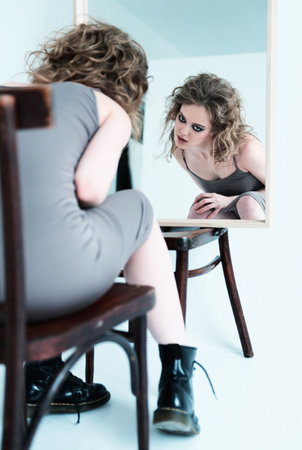 Portrait of strange freaky girl. Beautiful crazy young woman sitting on chair at the mirrorの写真素材