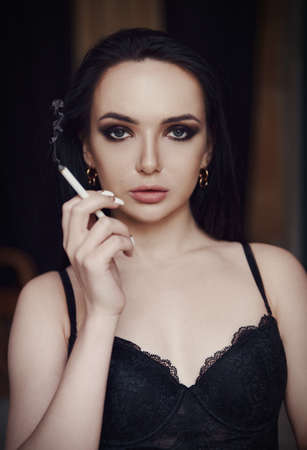 Lovely beautiful young woman in lingerie smoking cigarette. Portrait of beautiful girl in black braの写真素材