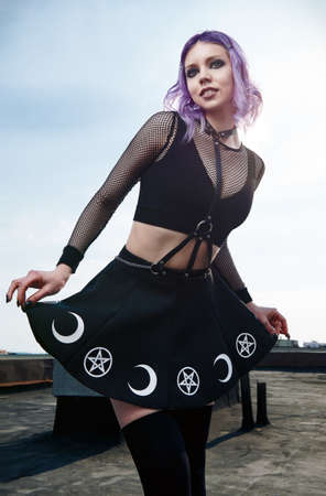 Portrait of pretty smiling gothic girl on the roof. Pastel goth with violet (purple) hair in black clothesの写真素材