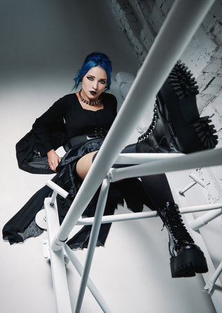 Gothic fashion: beautiful goth girl in black dress and boots lying on the floor near metallic construction. studio shotの写真素材