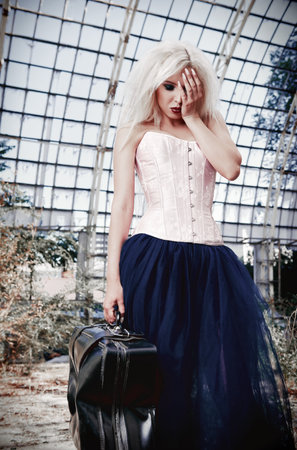 Portrait of the sad freak girl with old suitcase. Beautiful strange woman wearing corset, tights and tutu skirt in forsaken place. facepalm gestureの写真素材
