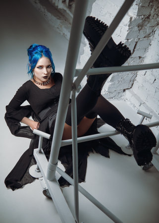 Gothic fashion: lovely goth girl in black dress and boots lying on the floor near metallic construction. Studio shotの写真素材