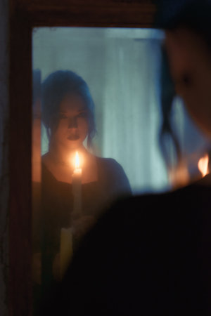 Indoors portrait of mysterious goth girl with candle. Blue-haired gothic woman looking into the old dirty mirror. Young witch. Vintage styleの写真素材