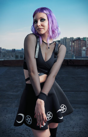 Portrait of cute smiling gothic girl on the roof at evening time. Pastel goth with violet (purple)...