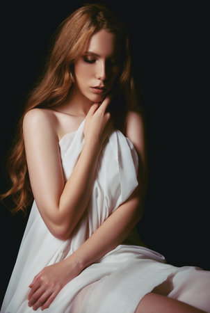 Dramatic portrait of the beautiful young sad girl against black background. Dismal woman among the darkの写真素材