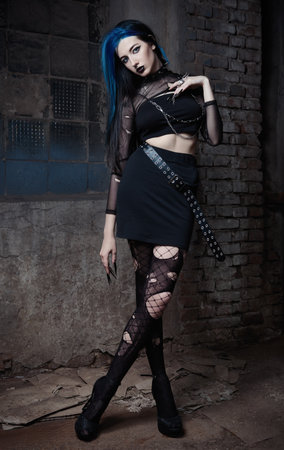 Outdoor portrait of cool goth (deathrock) girl dressed in black skirt, holey blouse and pantyhose. Dark beautyの写真素材