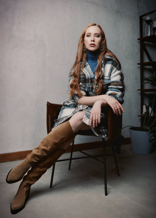 Retro fashion: beautiful young woman sits on chair. Vintage portrait of gorgeous girl in seventies styleの写真素材