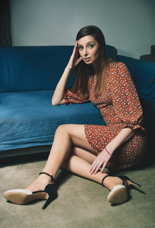 Retro (vintage) style portrait of a beautiful young girl sitting on the floor at the sofaの写真素材