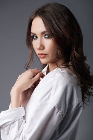 Studio portrait of the young woman. Cute girl dressed in white male shirt. Sweet lady against gray backgroundの写真素材