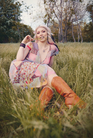 Outdoor portrait of the beautiful young boho (hippie) girl in forest (grove). Lovely smiling hippy woman sitting in grassの写真素材