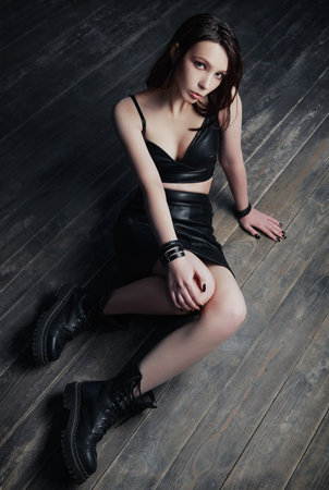 Studio fashion shot: beautiful sad goth girl sitting on a floor. Dark beauty: portrait of informal (rock) model in black topic, skirt and bootsの写真素材
