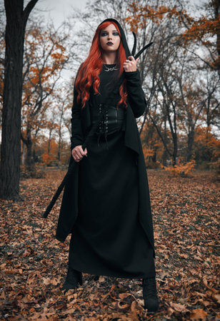 Halloween (Samhain) theme: a ginger (red-haired) witch with horned staff in the forest. Portrait of dangerous redhead mage in autumnal woodsの写真素材