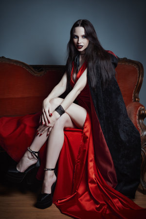 Dark beauty: seductive and gorgeous young woman in image of witch sitting on sofa. Portrait of vampire girlの写真素材