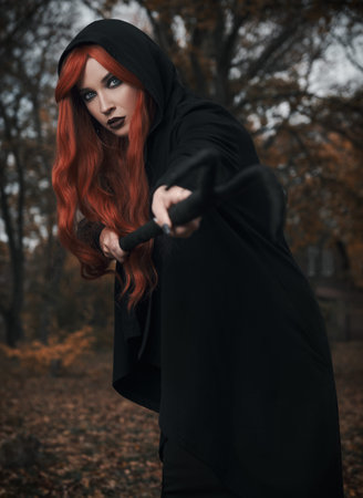 Halloween (Samhain) theme: a ginger (red-haired) witch with horned staff in the forest. Portrait of...
