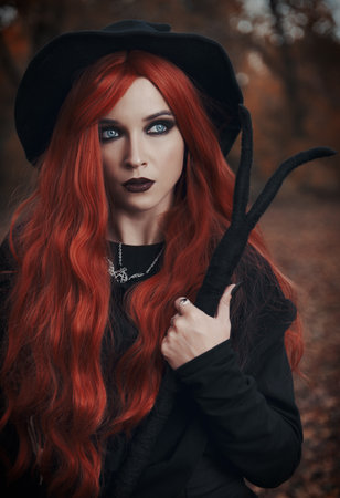 Halloween (Samhain) theme: a ginger (red-haired) witch with horned staff in the forest. Portrait of beautiful redhead sorceress in autumnal woodsの写真素材
