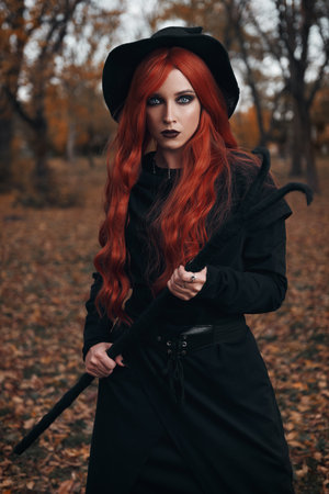 Halloween (Samhain) theme: a ginger (red-haired) witch with horned staff in the forest. Portrait of beautiful redhead hex in autumnal woodsの写真素材