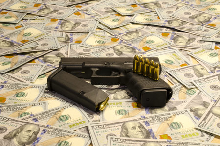 The weapon with blurred bullets laid down on blurred dollars.