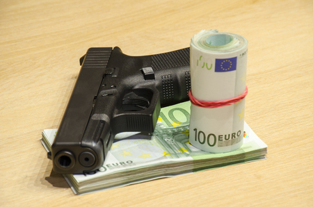 The pistol with bullets stays behind money with bllured wall backspace.の写真素材