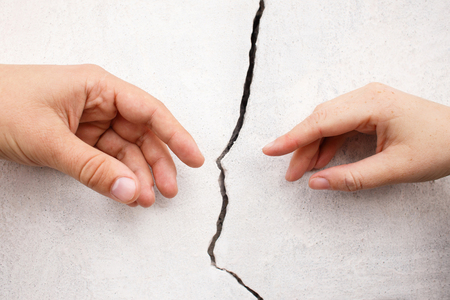 Hands stretching towards each other from otherside of crack of the wallの写真素材