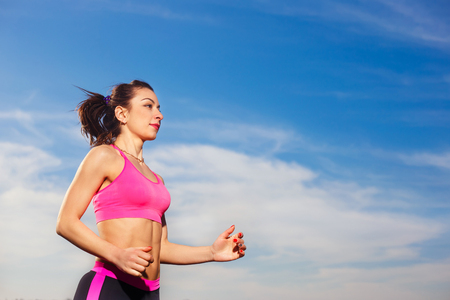 Young healthy woman running outdoor on the blue sky backgroundの写真素材