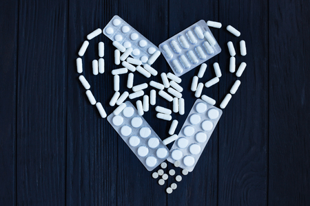 Tablets, pill capsules, pill blisters in shape of heart on blackの写真素材