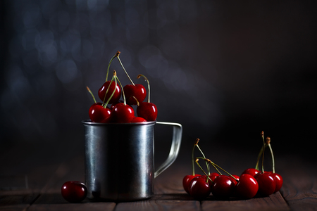 Fresh cherries in metal mug on table on dark backgroundの写真素材