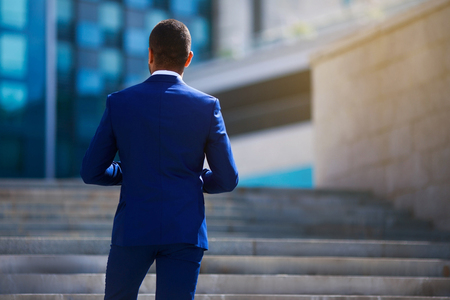 Back view of businessman thinking, standing outdoor looking at office buildingsの写真素材