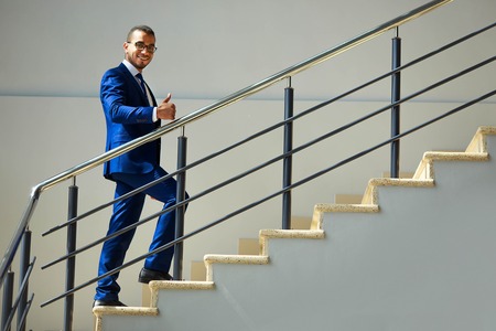 Stairs to success. Young smiling businessman climbs the stairs. Career conceptの写真素材