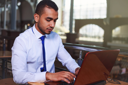 Young businessman working using laptop in interior, man typing on notebook computer at his workplace, flare lightの写真素材