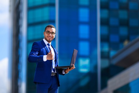 Business man in suit holding laptop while standing near office bの写真素材