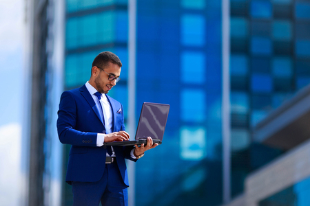 Competent business expert business man in suit holding laptop while standing near office buildingの写真素材