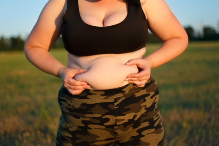 Overweight fat woman in camouflage pants standing outdoors showiの写真素材