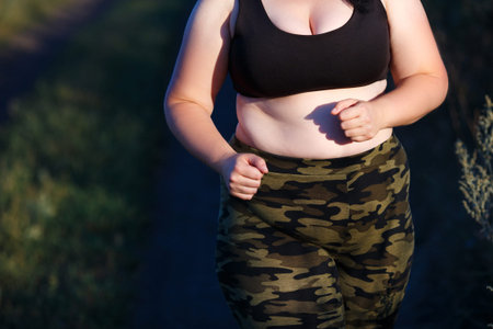 Overweight fat woman in camouflage pants and sporting bra jogginの写真素材