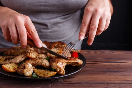 Woman tasting grilled chicken wings with fork and knife. Kitchenの写真素材