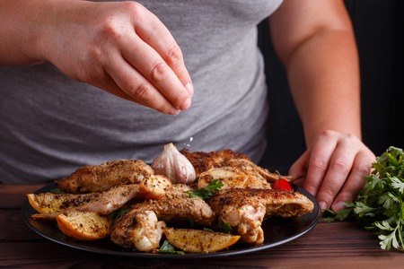 Woman adding salt to grilled chicken wings. Kitchen background,の写真素材