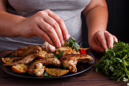 Woman decorating grilled chicken wings with parsley leaves. Kitcの写真素材