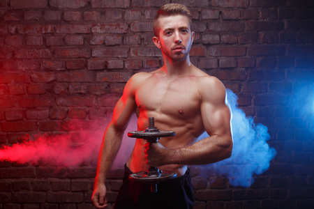 Strong athletic young man with huge muscles posing with dumbbellの写真素材