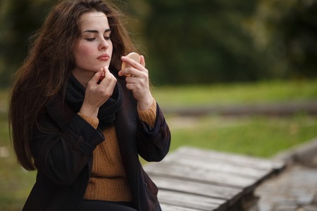 Young beautiful woman applying lipstick outdoorsの写真素材