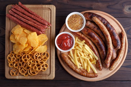 Appetizing beer snacks set for big company of friends. Grilled sausages and french fries with spicy tomato sauce and mustard, pretzel crackers, chips and salami on the board. Oktoberfest, pub conceptの写真素材
