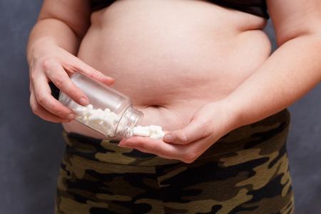 Close up of overweight fat woman taking slimming pills from bottの写真素材