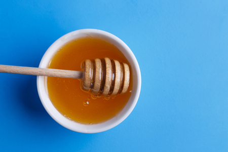 Honey with wooden honey dipper on blue background, view from aboの写真素材