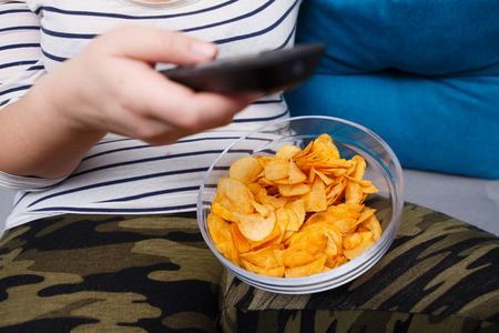 A bowl of chips while on the knees of fat overweight woman watchの写真素材