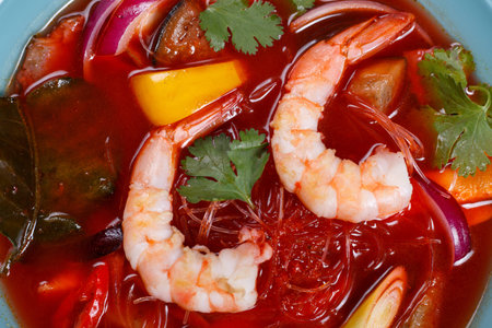 Appetizing red curry soup with prawns and rice noodles,close up.