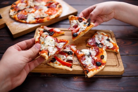 Eating pizza. Man and woman hands taking pizza slices served onの写真素材